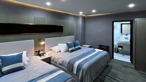Una camera d'albergo moderna con due letti, uno specchio grande e un bagno visibile attraverso una porta aperta.