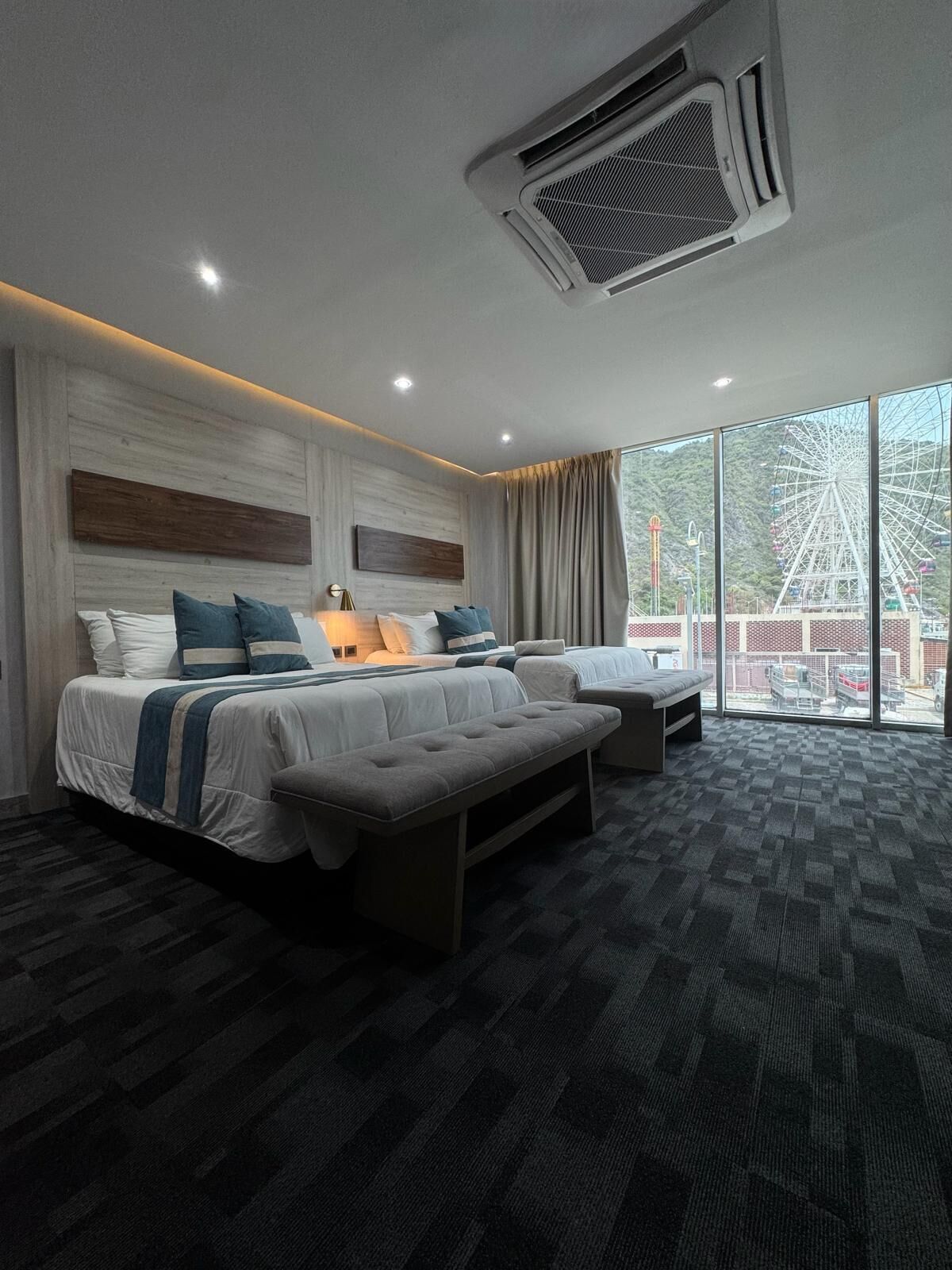 Een moderne hotelkamer met een groot bed, een bank en een kleine tafel. Er is een groot raam met uitzicht op een reuzenrad.