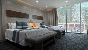 Een moderne hotelkamer met een groot bed, een bank en een kleine tafel. Er is een groot raam met uitzicht op een reuzenrad.