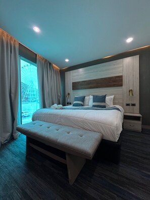 Une chambre moderne avec un grand lit, un banc et une vue sur une grande roue, visible par la fenêtre.