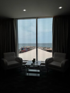 Une pièce avec deux fauteuils, une petite table sur laquelle se trouve une télécommande, et une vue sur la plage grâce à de grandes fenêtres.