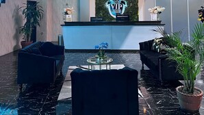 Una hall d'albergo con una reception, due divani, un tavolino da caffè e una scala.