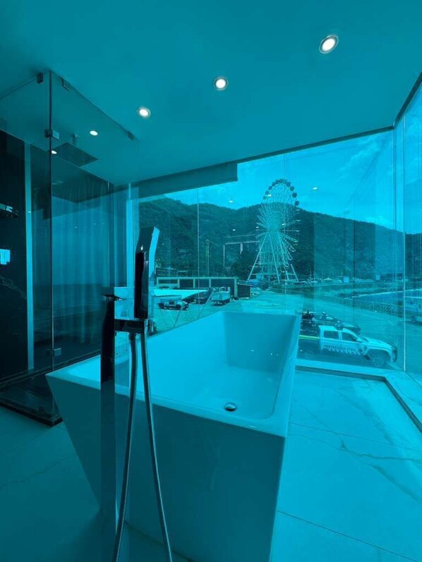Une salle de bain moderne dotée d’une grande baignoire, d’une cabine de douche en verre et offrant une vue sur une grande roue par de larges fenêtres.