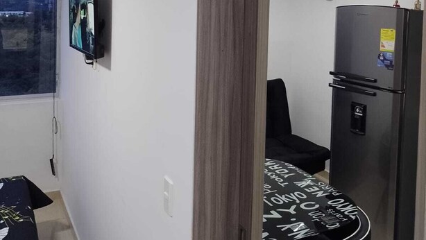 A modern kitchen with a refrigerator, a dining table with chairs, a TV mounted on the wall, and a window with blinds. - Oronegroapartahoteles Espectacular Apartaestudio Amoblado Armenia, Quindío (Quindío)