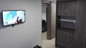 A room with a TV on the wall, a wooden cabinet, and a door leading to another room. - Oronegroapartahoteles Espectacular Apartaestudio Amoblado Armenia, Quindío (Quindío)