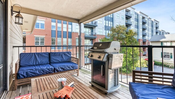 A balcony with a blue sofa, a grill, and a view of a brick building.
