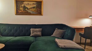 Un sofá verde con dos almohadones, una mesita y una lámpara sobre un escritorio de madera.