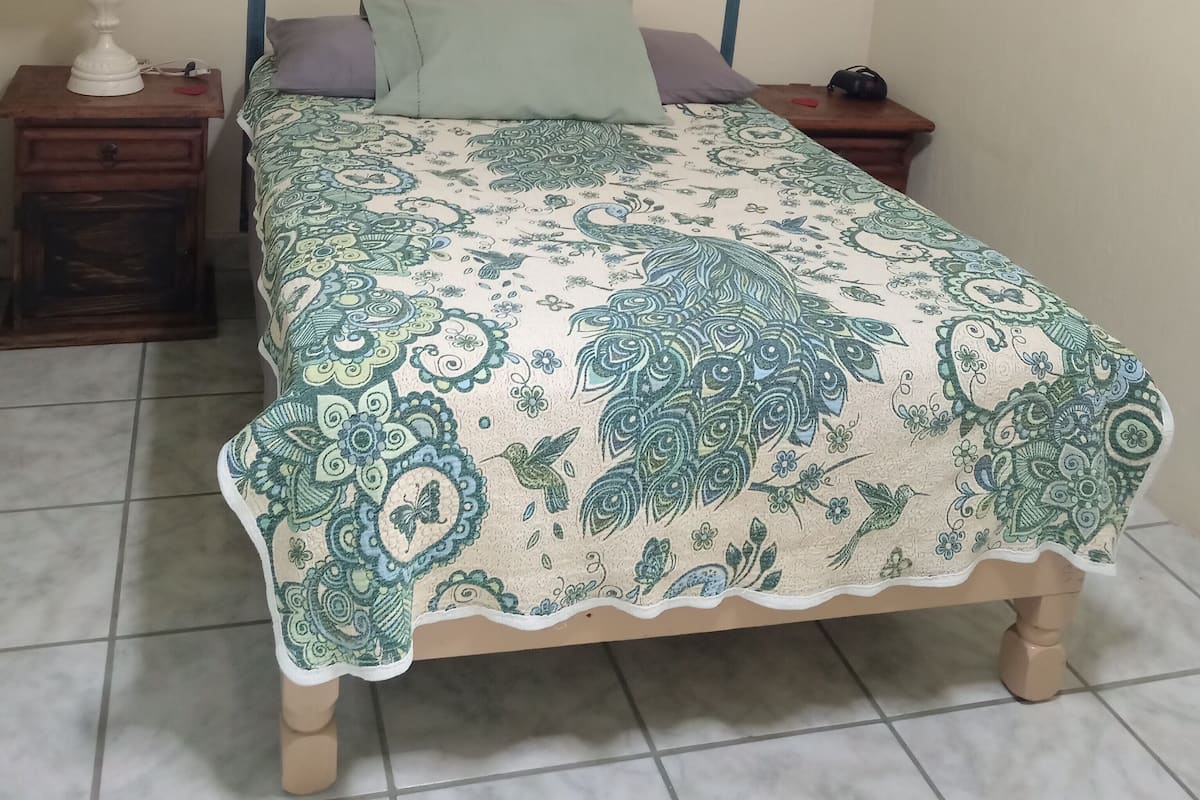 Un lit avec une tête de lit décorative, une table de chevet avec une lampe et un appareil de climatisation fixé au mur.