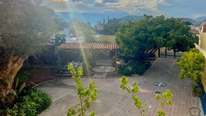 Un patio con estructura de techo de tejas, rodeado de follaje y un área pavimentada.