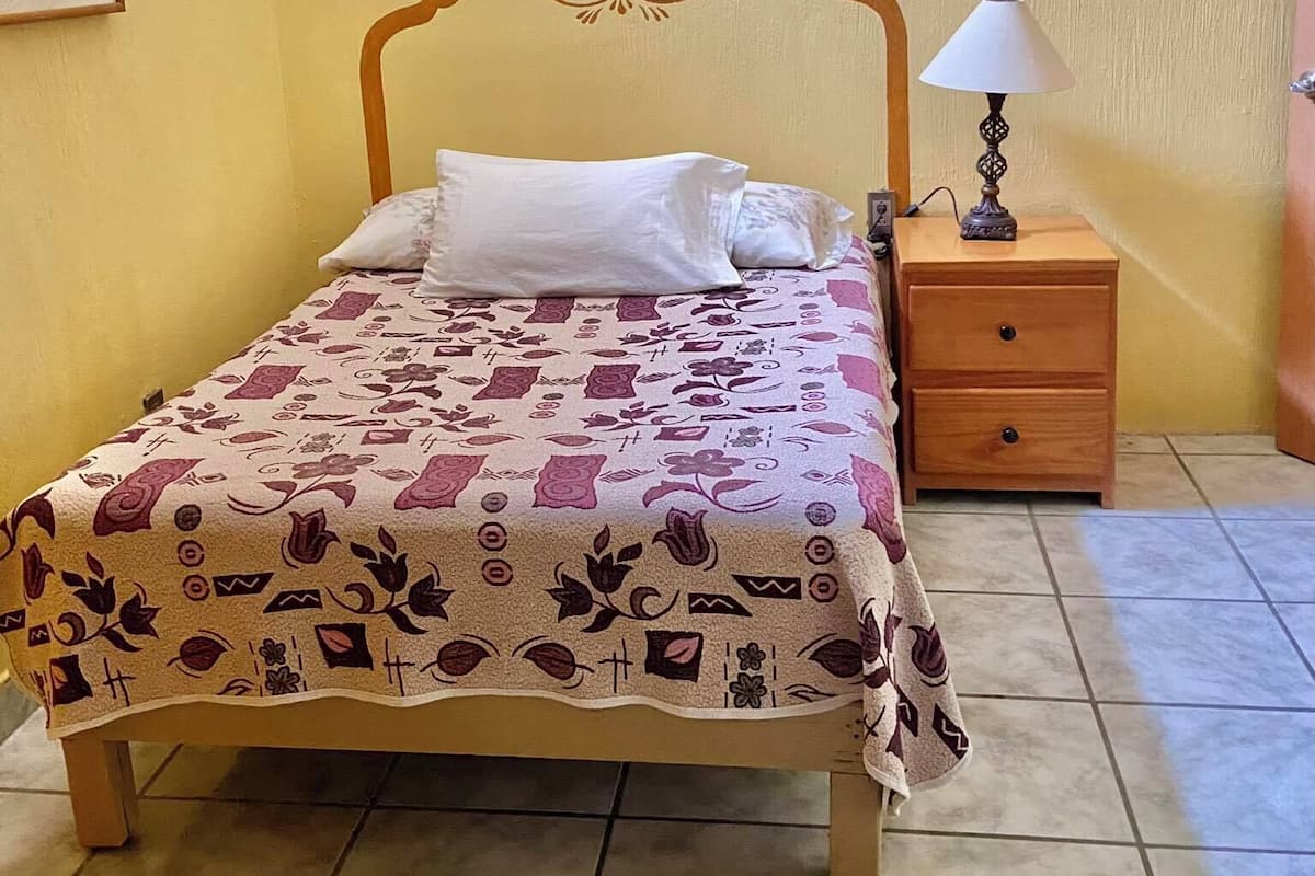 Une chambre à coucher avec un lit, une table de chevet et une lampe. Il y a trois petites fenêtres sur le mur.