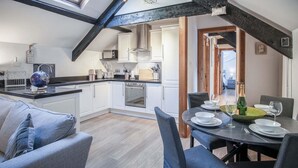 Una cocina moderna con armarios blancos, encimera negra y tragaluz. Hay un comedor con una mesa preparada para dos personas, un globo terráqueo y una botella de champán.