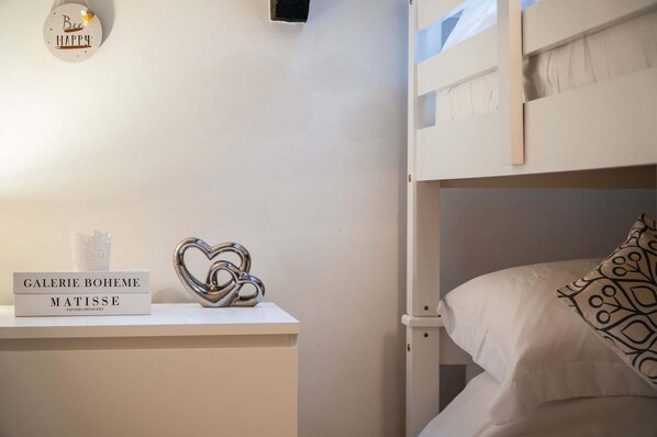 Una cama litera con una almohada estampada, un objeto decorativo con forma de corazón y un cartel con 'GALERIE BOHEME' y 'MATISSE PAPIRS DÉCOUPES' sobre una mesita de noche.