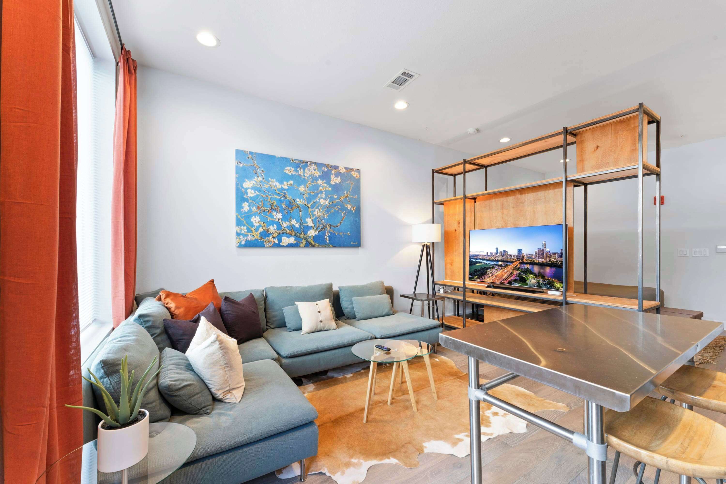Un salon moderne avec un canapé d’angle, une table basse en verre, un meuble TV en bois et un écran de télévision affichant un paysage urbain.