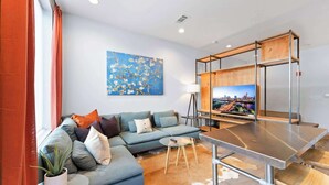A modern living room with a sectional sofa, a glass coffee table, a wooden TV stand, and a cityscape TV screen.