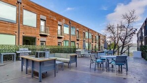A modern outdoor patio area with seating and a barbecue grill, adjacent to a building with large windows and balconies.
