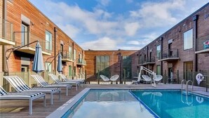 A swimming pool with lounge chairs and umbrellas, surrounded by brick buildings with balconies.