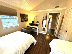 A bedroom with two beds, a desk, a chair, a mirror, and a window.