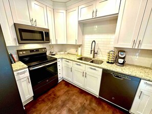 A kitchen with white cabinets, a microwave, stove, dishwasher, and a coffee maker.