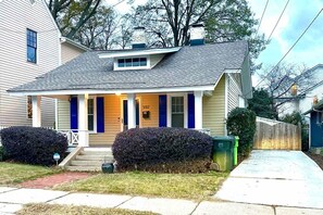 A single-story house with a front porch, a mailbox, and a green trash bin.