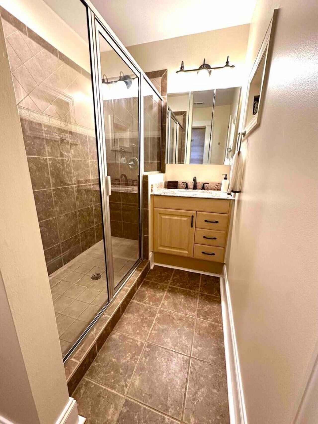 A bathroom with a glass shower enclosure, a vanity with a mirror, and tiled flooring.