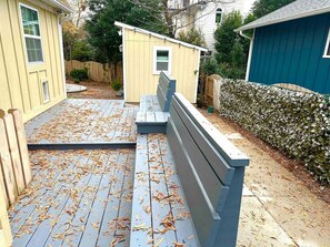Una terraza de madera con un banco, rodeada por una valla y un seto.