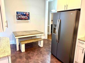 A kitchen with a wooden table and bench, a stainless steel refrigerator, and a wall-mounted television.