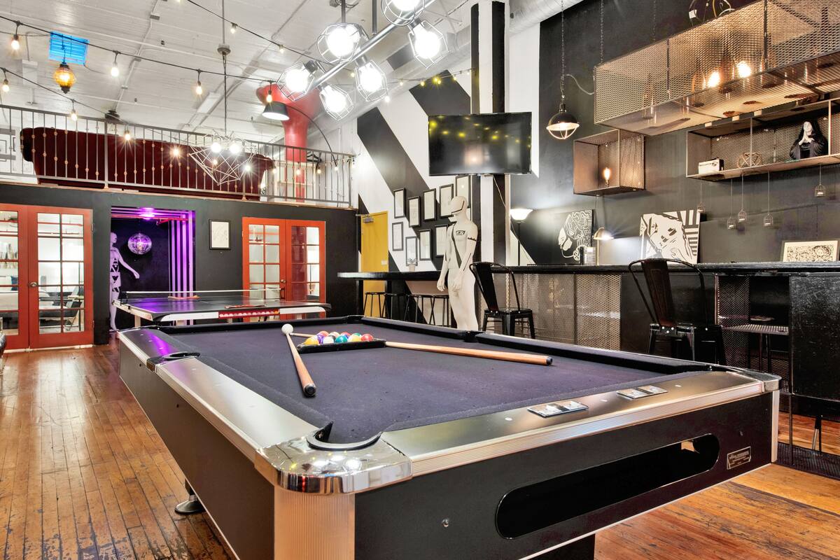 A pool table in a modern indoor setting with a high ceiling and exposed beams.