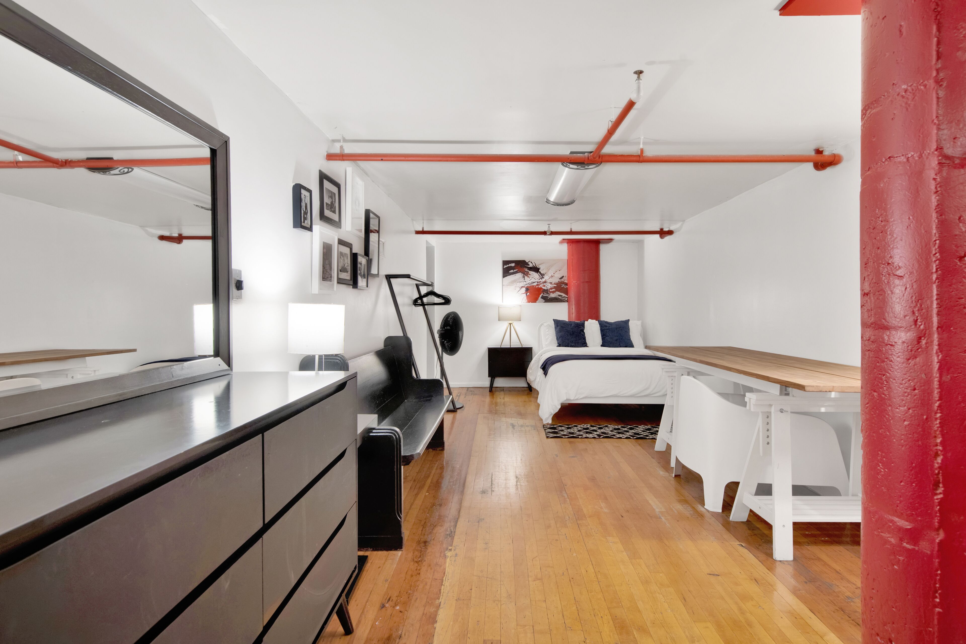 A modern bedroom with a wooden floor, a bed with white bedding, a black chair, a desk, and a large mirror.