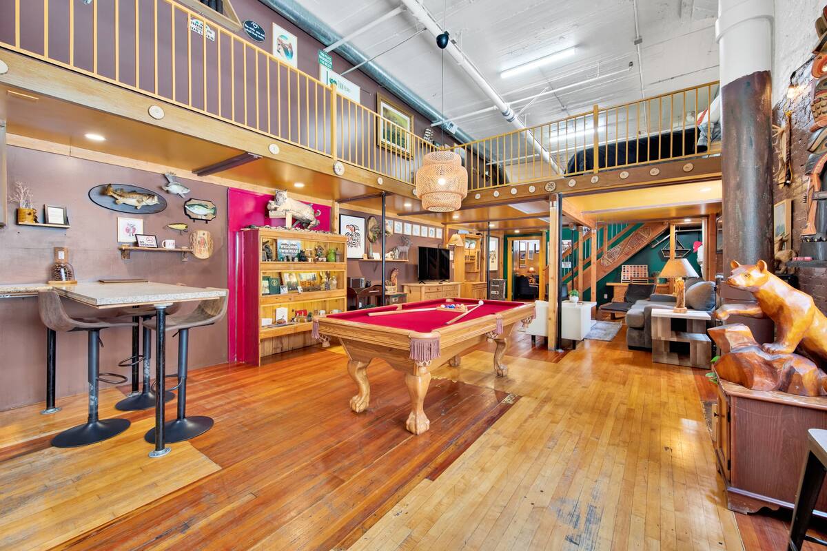 A spacious indoor area with a pool table, wooden flooring, and a mezzanine level with a railing.