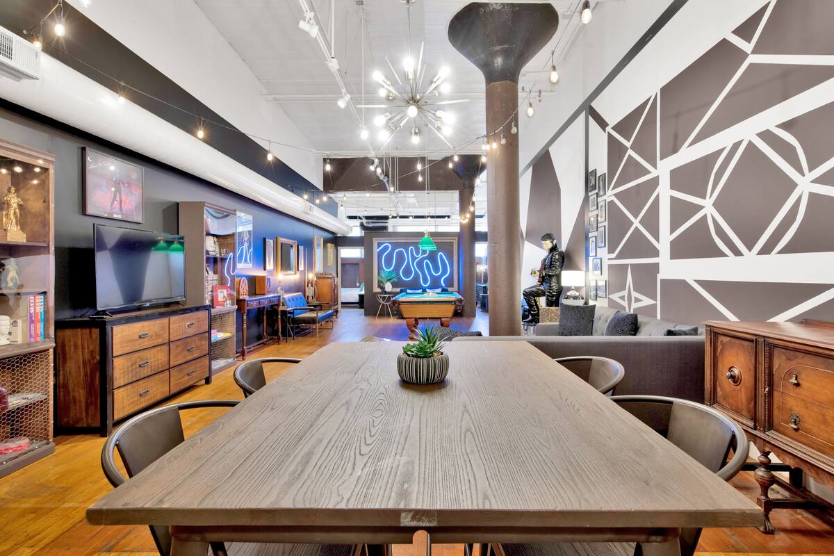 A modern interior with a wooden dining table, chairs, a neon sign, and a pool table.