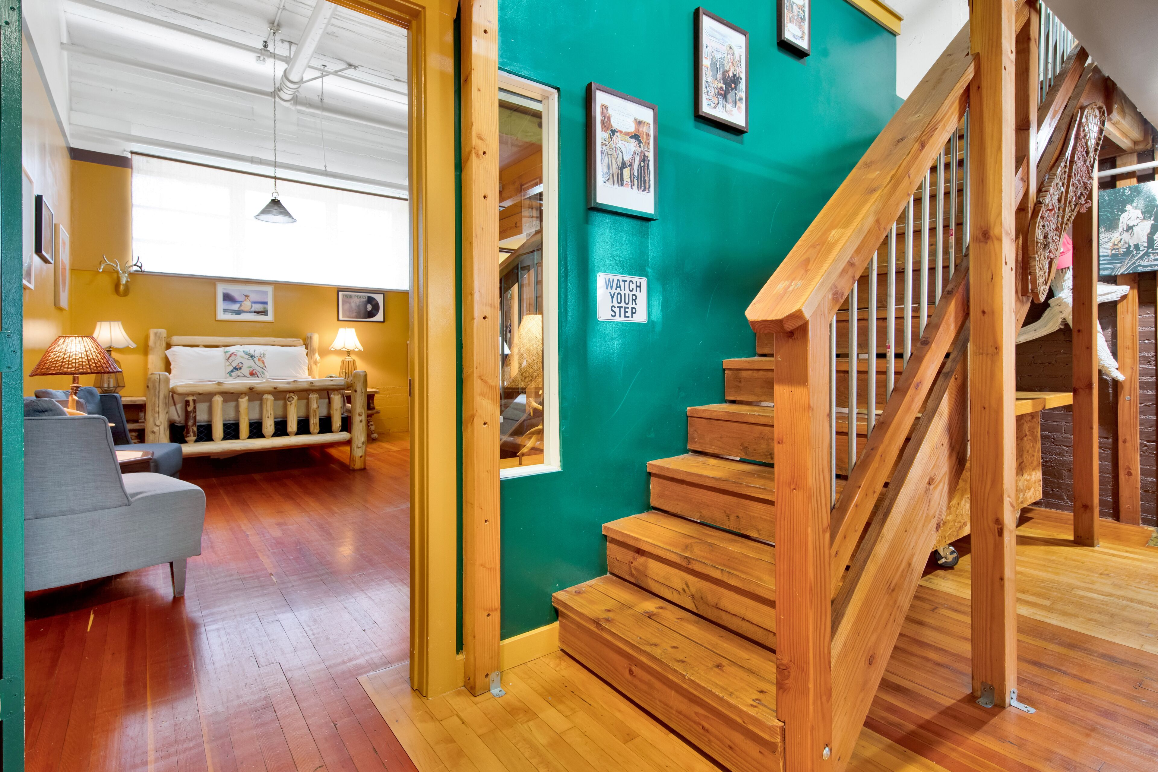 A room with wooden flooring, a staircase, a sofa, and a bed.