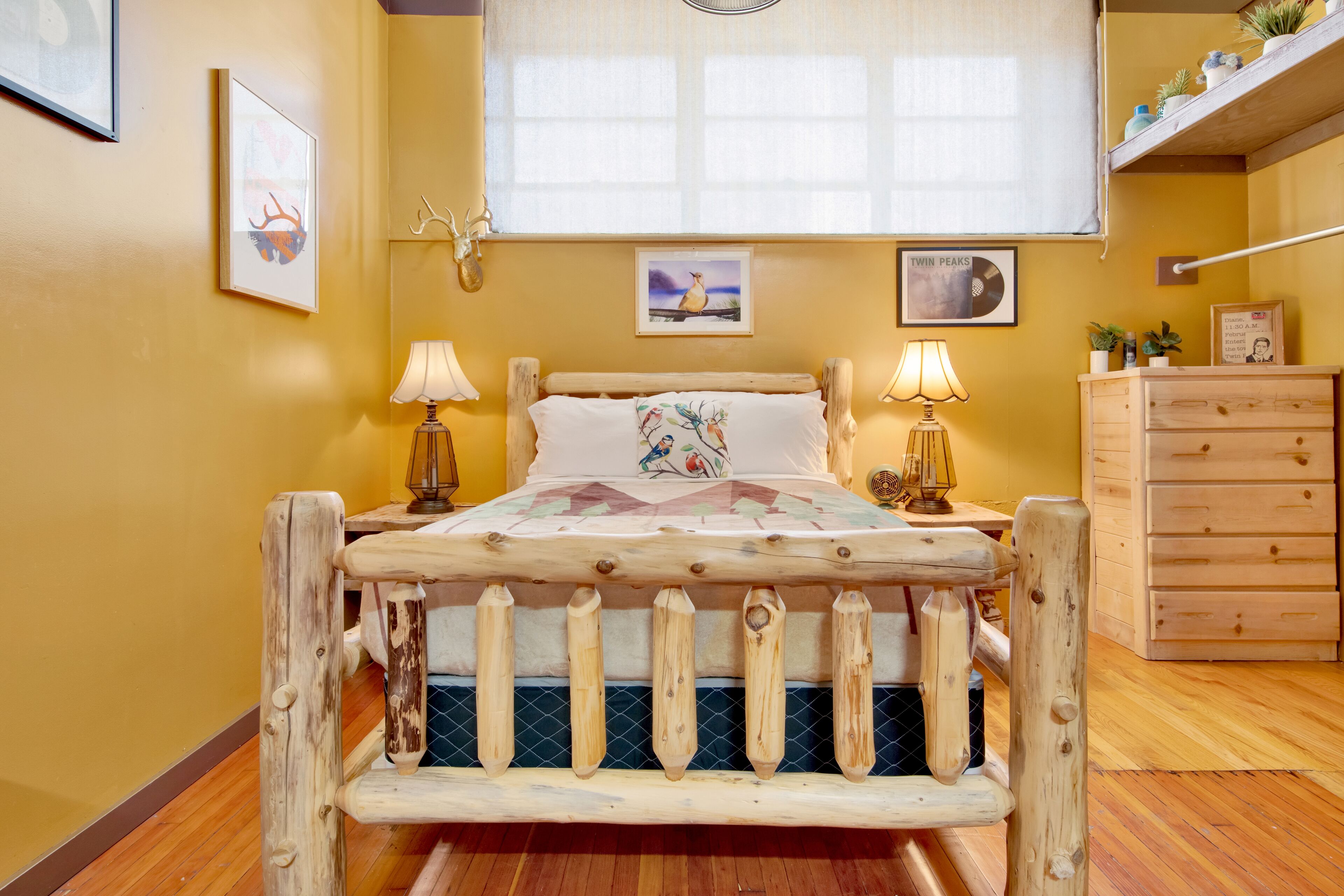Un dormitorio con estructura de cama de madera, dos lámparas de noche, un aparador y una ventana con cortinas.