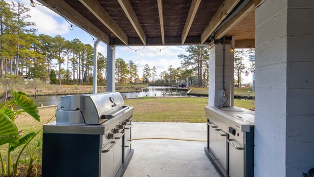 An outdoor kitchen with a grill and sink, surrounded by a concrete patio and a view of a lake and trees. - Private Waterfront Retreat with Breathtaking Views. Pet-friendly! (Belhaven)