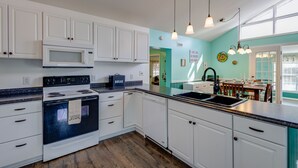 A kitchen with white cabinets, a microwave, an oven, a sink, and a dining area with a table and chairs. - Private Waterfront Retreat with Breathtaking Views. Pet-friendly! (Belhaven)