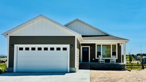 A modern two-story house with a garage, a covered porch with chairs, and a clear view of the surrounding landscape.