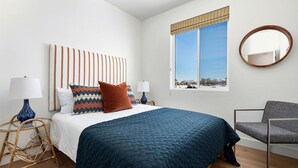 A bedroom with a bed, two bedside tables, a chair, a window with a view, and a wall-mounted mirror.