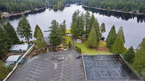 An aerial view of a parking lot with a basketball court, surrounded by trees and a lake. - Hot Tub - Game Garage. Peaceful 1 Level Lake Limerick Retreat with Fire-pit. (Shelton)