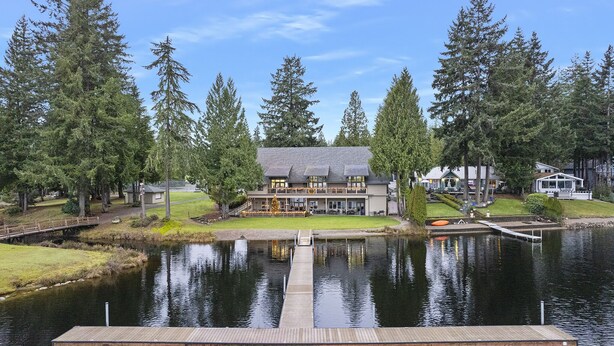 A lodge with a dock extending into a lake, surrounded by tall trees and a clear sky. - Hot Tub - Game Garage. Peaceful 1 Level Lake Limerick Retreat with Fire-pit. (Shelton)