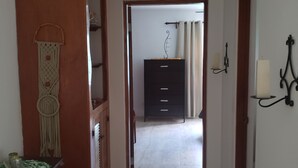 Ein Korridor mit einer Holztür links, einem schwarzen Schrank in der Mitte und einer weißen Wand mit einer schwarzen Wandleuchte rechts.