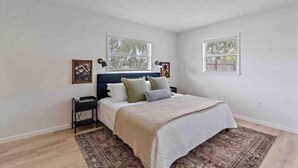 A bedroom with a bed, two bedside tables, a rug, and two windows. - The Peaceful Place (Sarasota)