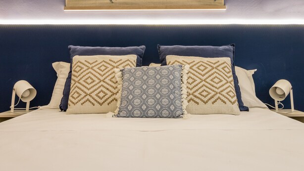 A neatly made bed with patterned pillows, a world map on the wall, and bedside lamps. - Ghiberti Apartments - Persian Blue (Trieste)