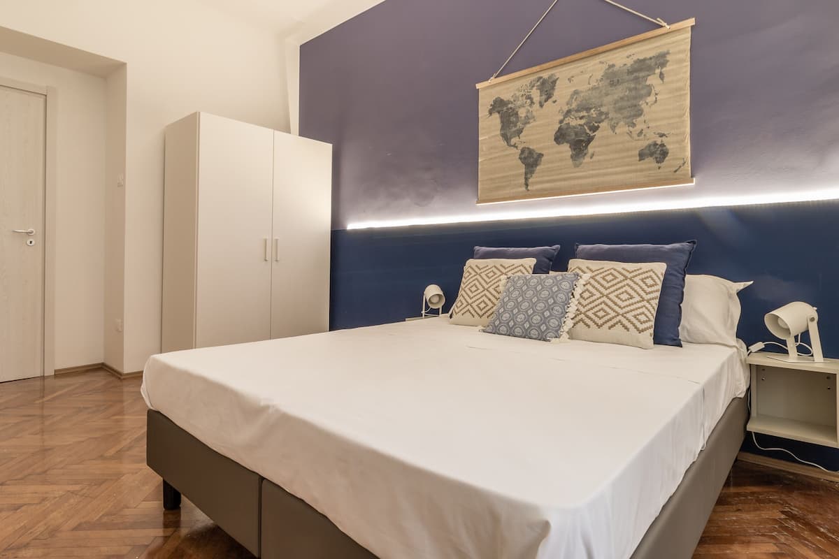 A bedroom with a bed, a wardrobe, a world map on the wall, and a bedside table with a lamp.