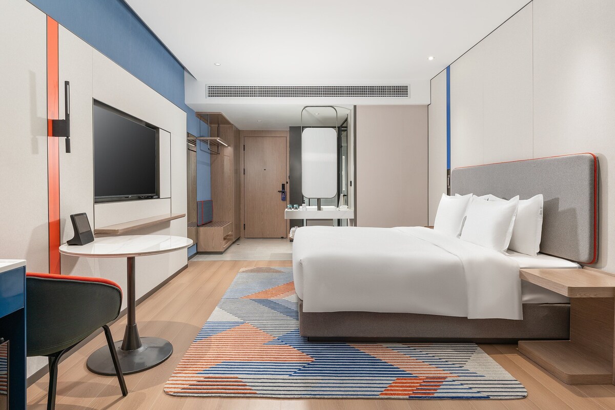 Een moderne hotelkamer met een bed, bureau, stoel, televisie en een badkamer zichtbaar door een geopende deur.