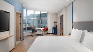 A hotel room with a large bed, a TV, a dining table with chairs, and a view of the city through large windows. - Holiday Inn Express Shangri La by IHG (Deqin)