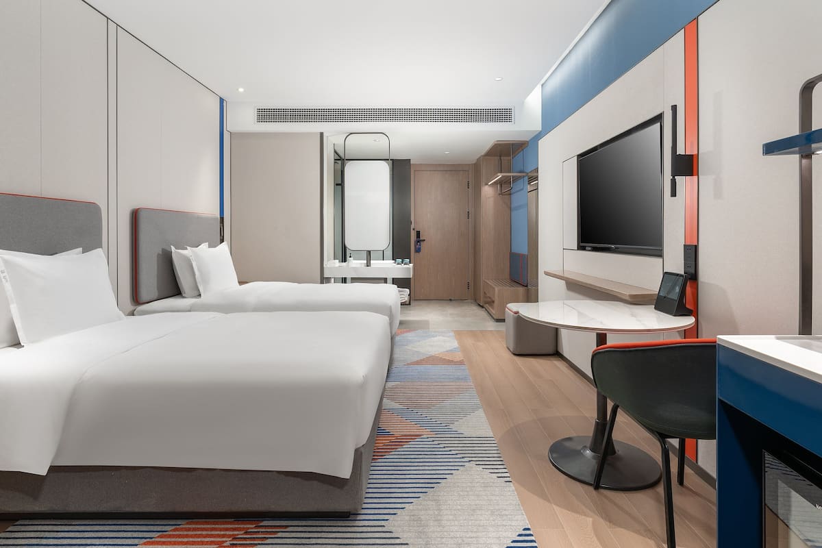 A modern hotel room with a large bed, a desk with a chair, a TV, and a bathroom.