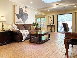 A spacious living room with a leather couch, a coffee table, and a large window offering a view of the outdoors.