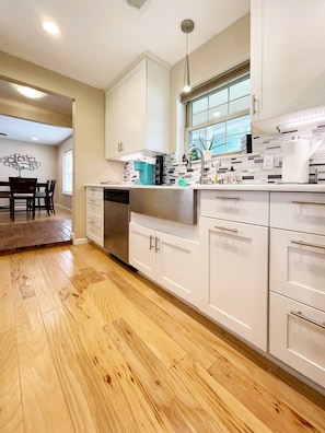 A modern kitchen with white cabinets, a stainless steel dishwasher, and a window above the sink.