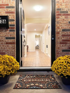A hotel entrance with a brick facade, a welcome mat, and yellow flowers.