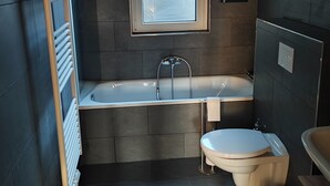 Een moderne badkamer met een bad, toilet en wastafel.