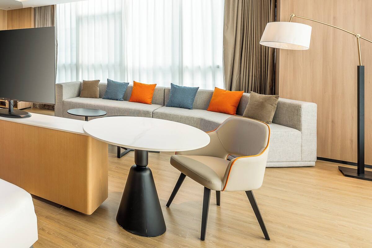 A modern hotel room with a sofa, a round table, a TV, and a lamp.